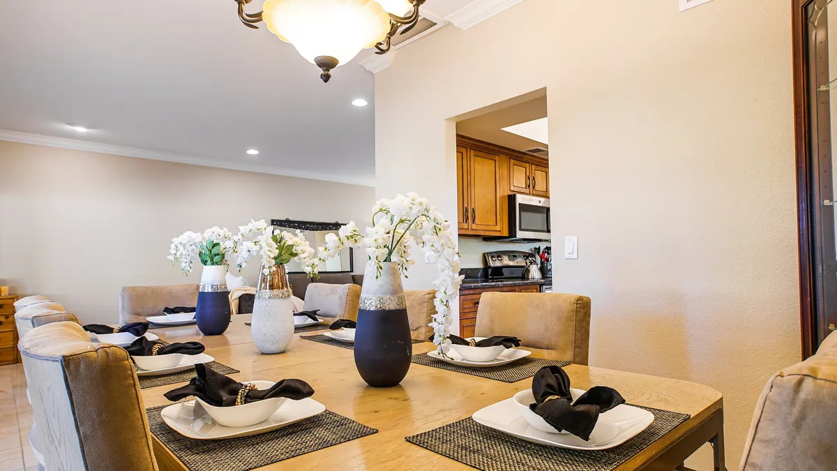 A beautifully set dining table, adorned with floral arrangements and illuminated by a chandelier. The kitchen entrance is visible in the background, emphasizing easy access and flow for shared meals and celebrations.