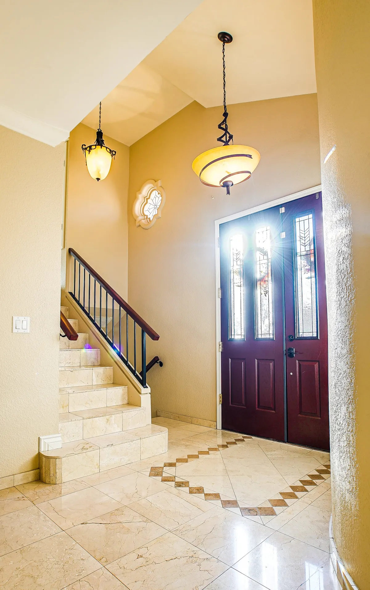 This interior shot captures the home's stylish double front doors, a grand staircase, a chandelier, and a decorative window. The entryway is bright and welcoming, evoking the feeling of arrival and the start of a new experience.