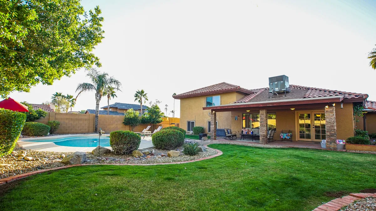 This image showcases a sparkling swimming pool surrounded by inviting outdoor seating and a beautifully landscaped garden. The pool area is the focal point, with ample space for sunbathing, swimming, and relaxing. The lush greenery and clear desert sky set a vibrant, welcoming tone for outdoor enjoyment.