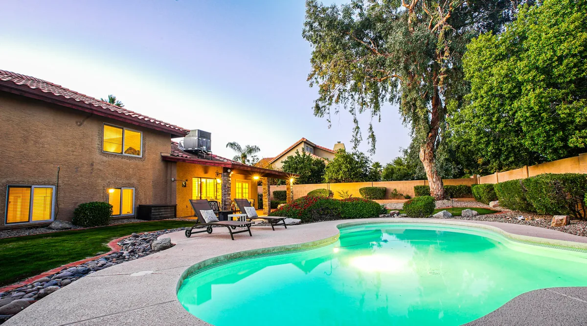 This image features a sparkling swimming pool surrounded by lounge chairs and a landscaped garden, with the house's exterior in view. The inviting scene highlights both relaxation and the opportunity for outdoor recreation, with ample space for sunbathing or quiet work sessions by the water.