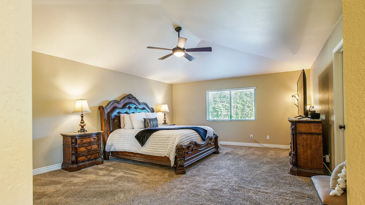 This image shows a large wooden bed flanked by nightstands with lamps, set in a serene, sunlit bedroom. The window allows natural light to fill the space, creating an inviting and restful atmosphere.