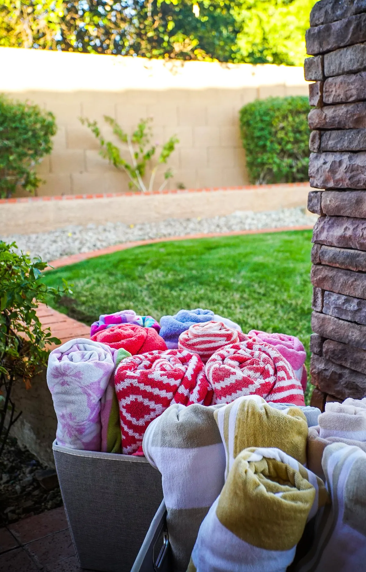 Colorful towels are neatly arranged on lounge chairs beside a vibrant green lawn and stone wall, creating a cheerful spot for family gatherings, sunbathing, or playful afternoons outside.