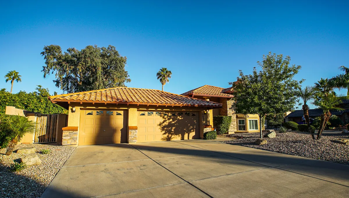 An inviting exterior shot showcasing the home's garage door, tiled roof, palm trees, and landscaped yard—an ideal first impression for arriving guests or heading out to nearby golf courses and sporting events.