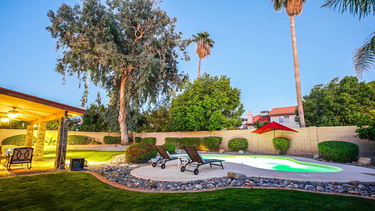 A stylish pool area with multiple lounge chairs, a large tree for shade, and a striking red umbrella. The tranquil scene evokes a sense of leisure and provides ample space for group gatherings or quiet relaxation.