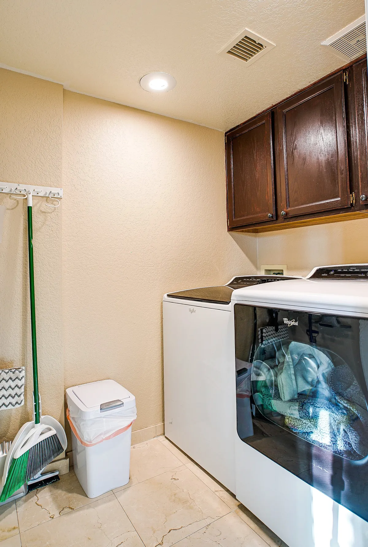 A tidy laundry room featuring a washer and dryer, storage cabinets above, and a selection of cleaning supplies. The scene exudes practicality and ease, reflecting everyday home convenience.
